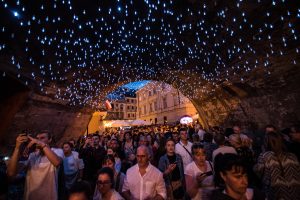 Evening crowd under an archway with blue hanging lights at a city festival