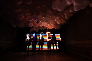 Light-painted word 'SUPER' in front of rainbow stripes and balloons